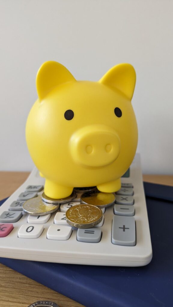 Yellow savings piggy bank stood on a calculator with coins at its feet