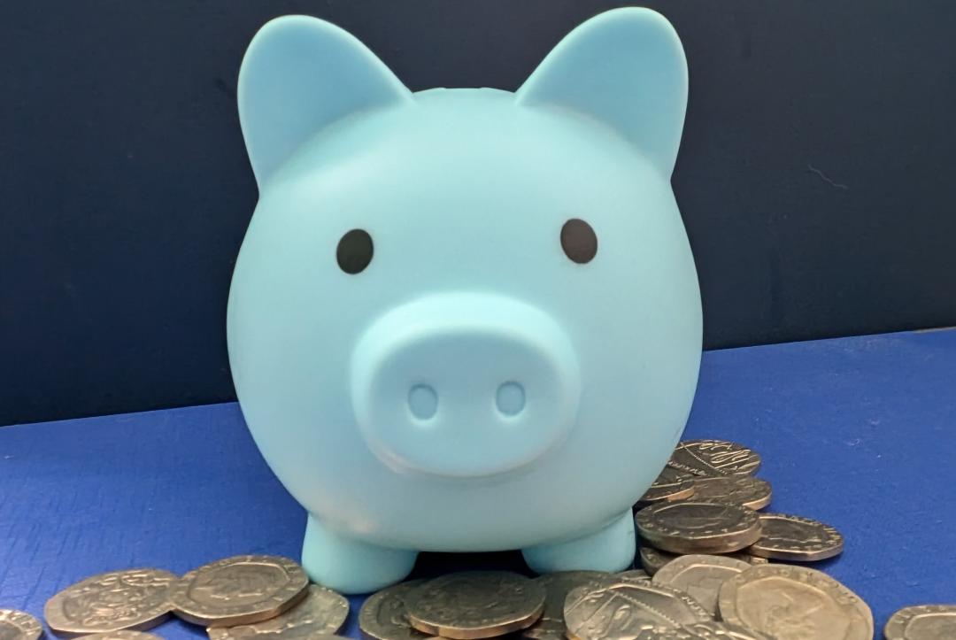 Blue money box pig with twenty pence coins at its feet